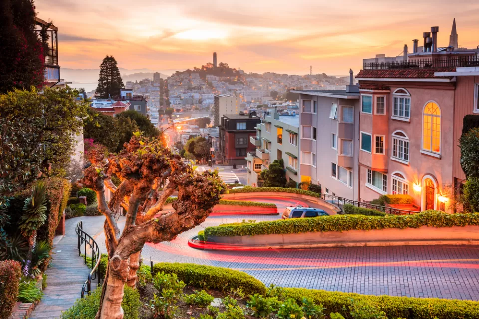 View of downtown San Francisco from top of windy street at sunset with Coit Tower in distance
